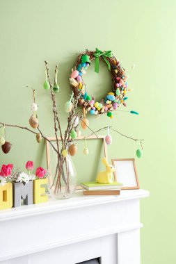 Dekorlu şömine rafı ve yeşil duvarlı Paskalya çelengi.