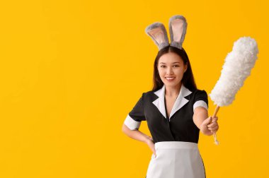 Tavşan kulaklı genç Asyalı oda hizmetçisi ve sarı arka planda toz bezi. Paskalya kutlaması
