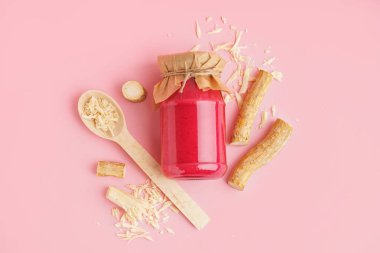 Kavanozda pancar soslu yaban turpu sosu ve pembe arka planda yer turpu. Üst görünüm