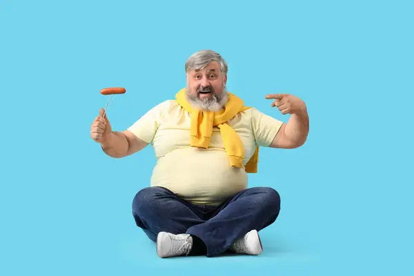 stock image Mature man pointing at tasty sausage on blue background