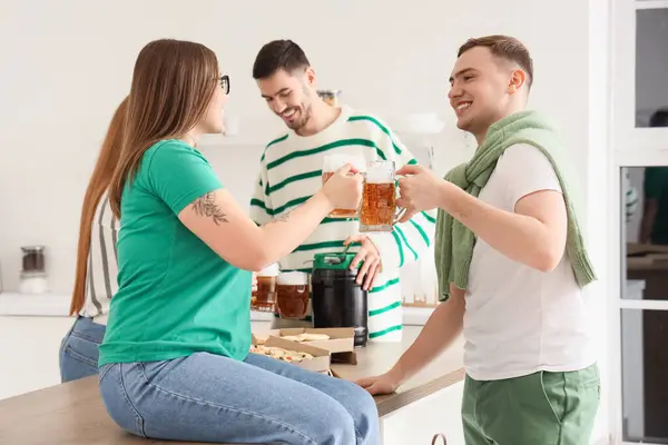 Young friends with beer celebrating St. Patrick's Day in kitchen