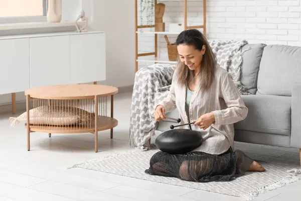 stock image Beautiful mature woman with sticks playing glucophone on carpet at home