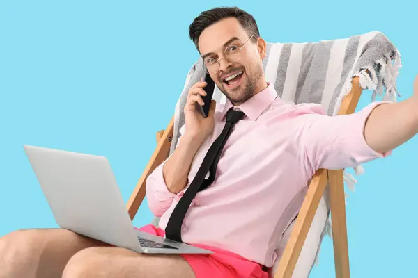 Vtipný Podnikatel Notebookem Sedí Lehátku Mluví Mobilním Telefonem Modrém Pozadí — Stock fotografie