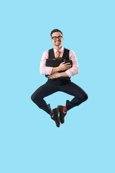 Funny businessman with briefcase jumping on blue background