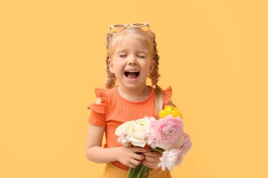 Sarı arka planda bir buket güzel ranunculus çiçeğiyle duygusal küçük kız.