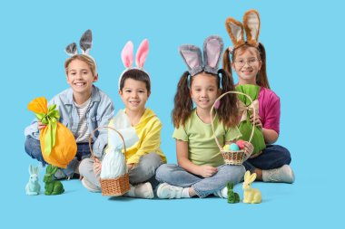 Mavi arka planda oturan tavşan kulaklı küçük çocuklar.