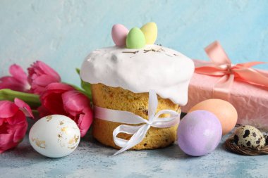 Lezzetli dekore edilmiş Paskalya pastası, çiçekler ve renkli arkaplanda boyanmış yumurtalar.