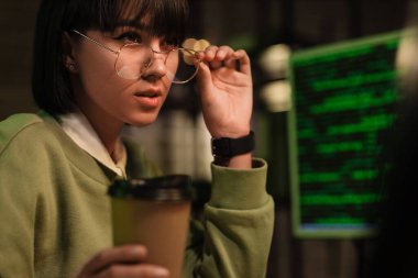 Elinde kahve fincanı olan kadın programcı gece ofiste bilgisayarla çalışıyor, yakın plan.