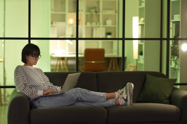 Geceleri koltukta dizüstü bilgisayarla çalışan kadın programcı.