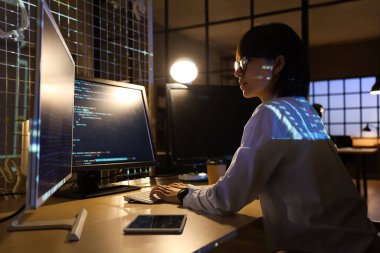 Genç bayan programcı geceleri ofiste bilgisayarla çalışıyor.