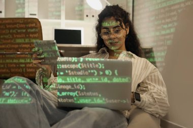 Armut çantasının üzerinde cihazları olan ve gece ofiste kod projeksiyonu yapan Afro-Amerikalı bir kadın programcı.