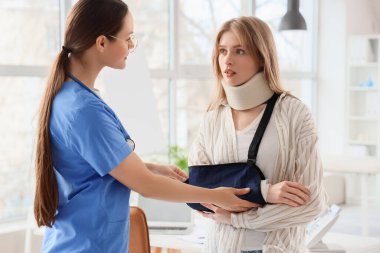 Injured young woman with broken arm after accident visiting doctor in clinic clipart