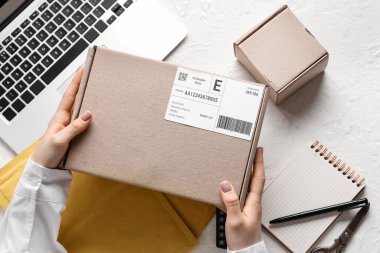 Beyaz masada dizüstü bilgisayarlı ve zarflı karton paketleri tutan kadın eller.