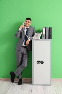 Yeşil duvarın yanında telefon kulübesi ve klasörleri olan mutlu genç adam konuşuyor.