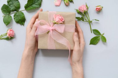 Mavi arka planda güller olan güzel hediye kutusunu tutan kadın eller.