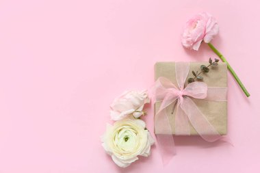 Pembe arka planda çiçekler olan paketlenmiş hediye kutusu