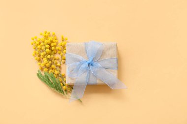 Sarı arka planda mimoza çiçekleri olan zarif paketlenmiş hediye kutusu.