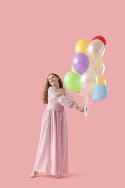 Pembe arka planda balonları olan genç bir kadın.