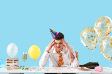 Mavi arka plandaki doğum günü partisinden sonra masada akşamdan kalma genç bir iş adamı.