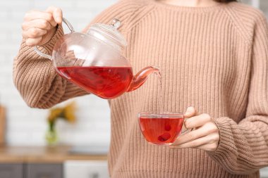 Genç bir kadın mutfakta çaydanlıktan fincana siyah çay dolduruyor.