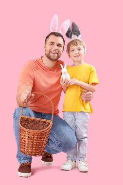 Küçük çocuk ve babası pembe arka planda sepeti olan tavşan kulaklı. Paskalya kutlaması