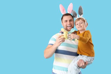 Babası tavşan kulaklı küçük bir çocuk ve mavi arka planda Paskalya tavşanları.