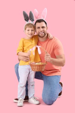 Pembe arka planda Paskalya yumurtaları olan tavşan kulaklı küçük çocuk ve babası