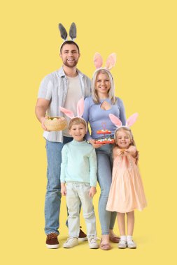 Sarı arka planda Paskalya yumurtaları olan tavşan kulaklı mutlu bir aile.