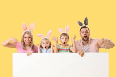 Sarı arka planda boş posteri olan tavşan kulaklı bir aile. Paskalya kutlaması