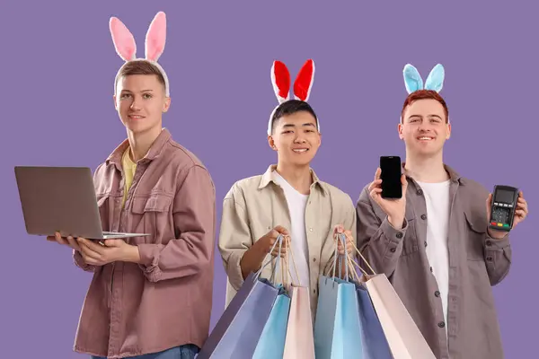 Junger Mann Hasenohren Mit Gadgets Und Einkaufstaschen Auf Fliederfarbenem Hintergrund — Stockfoto