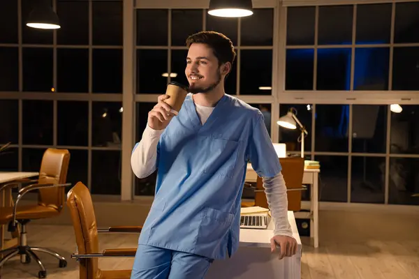 Male nurse with cup of coffee at hospital in evening