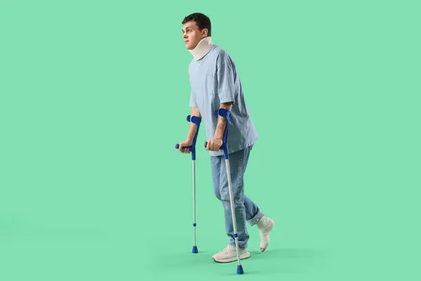 Injured young man after accident with crutches walking on green background