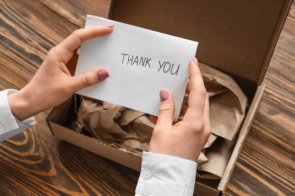 Женщина кладет письмо с благодарностью в картонную упаковку на деревянный стол