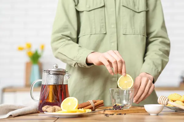Young woman putting lemon in cup of tea in kitchen