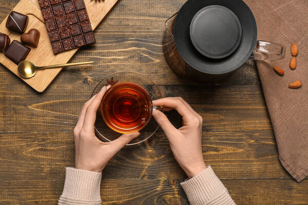 Female hands holding cup of tea and teapot on wooden background