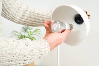 Genç adam evdeki masa lambasında ampulü değiştiriyor.