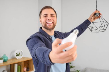 Genç adam evdeki lambada ampul değiştiriyor.