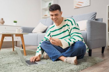 Evde dizüstü bilgisayar kullanan bir şişe CBD yağı taşıyan genç adam.