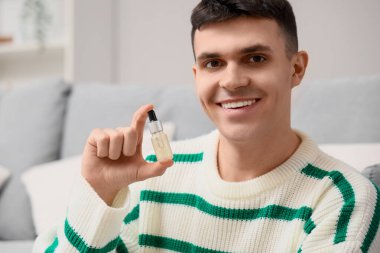 Evinde bir şişe CBD yağı olan genç adam, yakın plan.