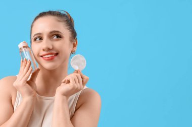 Mavi arka planda mikiler suyu ve pamuk pedi olan genç kadın, yakın plan.