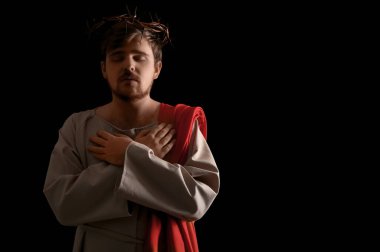 İsa cüppeli adam ve dikenli taç siyah arka planda ışıkla el ele geçiyor.