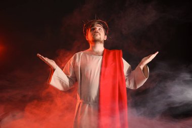 İsa cüppeli bir adam ve dikenli bir taç uzanan elleri siyah arka planda dumanla