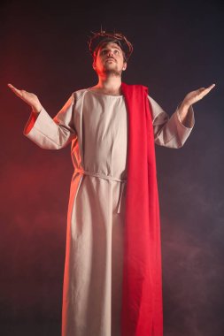 İsa cüppeli bir adam ve dikenli bir taç uzanan elleri siyah arka planda dumanla