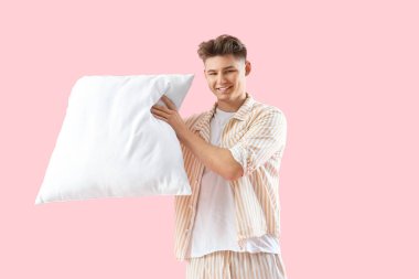 Pembe arka planda yumuşak yastıklı pijamalı genç adam.