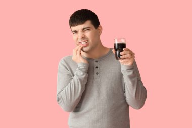 Young man with glass of soda suffering from toothache on pink background clipart