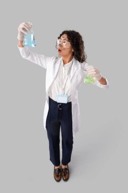 Afro-Amerikalı kadın kimyagerin hafif arka planda şişeleri ile şok oldu.