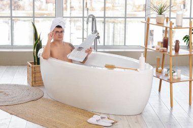 Elinde gazete olan yakışıklı adam evde banyo yapıyor.
