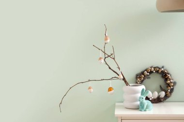 Ağaç dalları olan vazolar, Paskalya yumurtaları ve çelenkler ışık duvarının yanında.