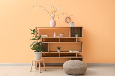 İçinde ağaç dalları olan vazolar ve odada bej duvarın yanındaki rafta Paskalya yumurtaları var.