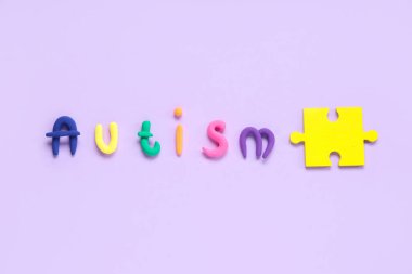 Eflatun arkaplan üzerine yapboz içeren plastikten yapılmış kelime AUTISM